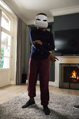 Obraz premium African male youth wearing white virtual reality headset, standing on rug in living room near TV