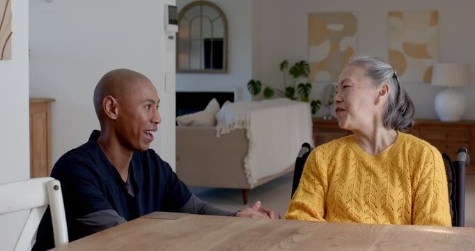 Senior Asian woman yellow knit, African American aide after glance touching hand to comfort