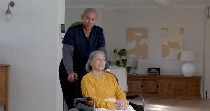 Senior Chinese woman in yellow knit with aide pushing wheelchair to table at home fixing blanket