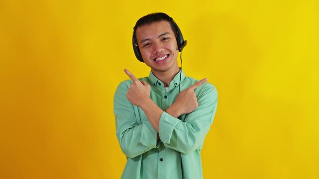 Friendly Asian customer service agent wearing headset pointing in both directions isolated on yellow backdrop for choosing concept