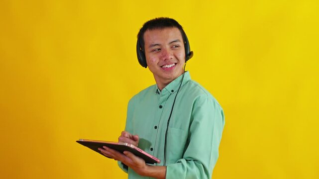 Asian call center agent using tablet while speaking to side profile isolated on bright yellow background