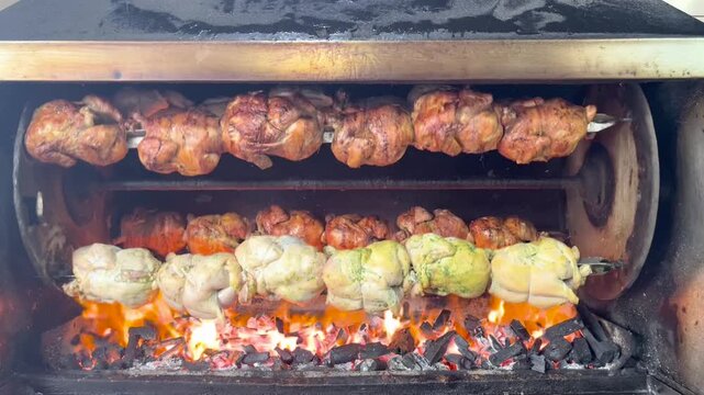 Whole chickens rotating on a charcoal rotisserie, slowly browning over glowing embers, showcasing the traditional fire‑cooking process and the warm atmosphere of a rustic kitchen.