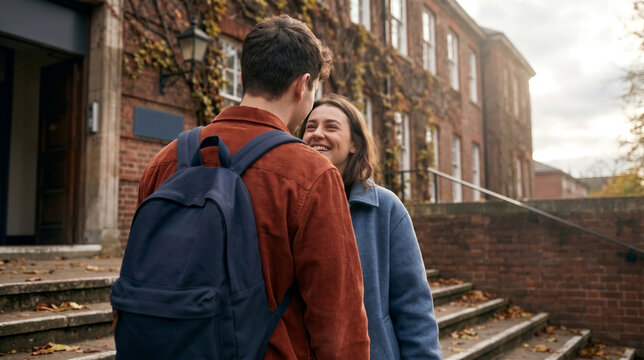 Young couple looking at each other with love and smiling while standing on the steps of a university building