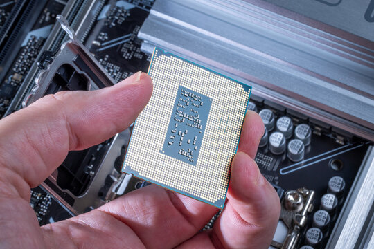 CPU with LGA socket held in technician's hand. Background shows motherboard during PC assembly or upgrade. Visible motherboard components. High-end computer parts