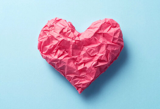 Crumpled pink paper shaped like a heart on light blue background