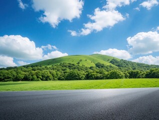Fototapeta na wymiar Empty asphalt road leads to green hill under blue cloudy sky. Rich trees border grassy field. Scenic landscape perfect for travel, nature, drive themes.