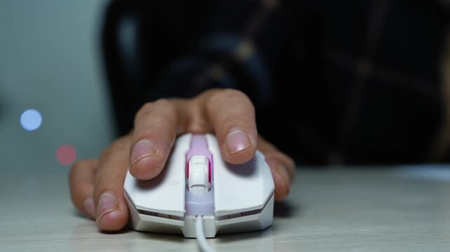 Hand clicking a wired computer mouse on desk, Close-up of a hand using a wired computer mouse on a desk, showing online work, gaming, browsing, and technology use in a dark indoor setting.
