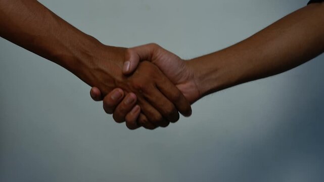 Handshake showing trust and partnership, Close-up of two people shaking hands against a soft gray background, showing agreement, trust, partnership and mutual support.