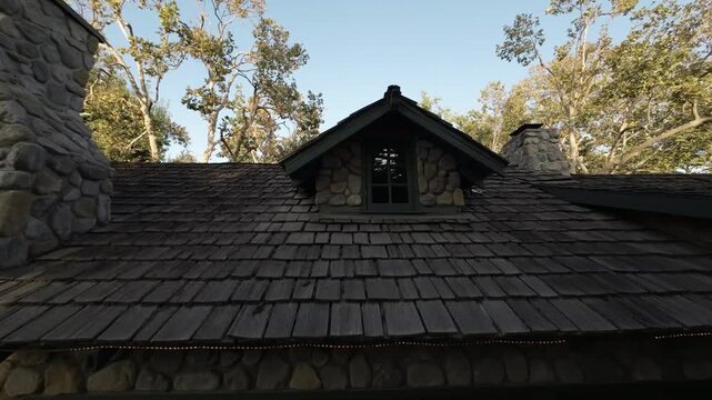 Wood shingle roof and stone dormer of a cottage against blue sky