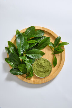 Green tea leaves and powdered tea arranged on a wooden tray, presenting two forms of the ingredient for tea packaging and natural product concepts.