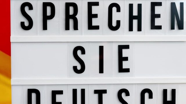 Lightbox with text SPRECHEN SIE DEUTSCH DO YOU SPEAK GERMAN National symbol of Germany. German wave silky flag background. Concept of education and learning languages 