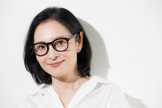 [白背景]眼鏡をかけた50代女性のポートレート、知的で落ち着いた印象のミドル世代とアイウェアのイメージ クローズアップ 　カメラ目線