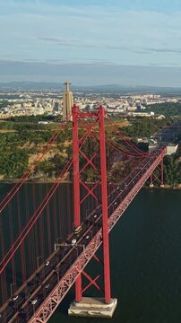 Aerial view of the red 25 April Bridge crossing the Tagus River with the Cristo Rei monument and Almada cityscape in the background. 
