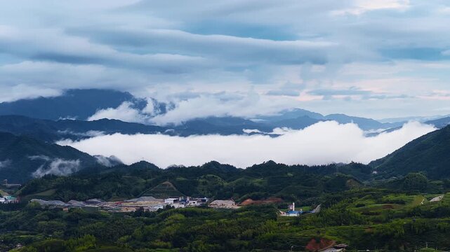 Green mountain slopes surround a valley filled with thick white fog under an overcast cloudy sky, illuminated by soft daytime light.