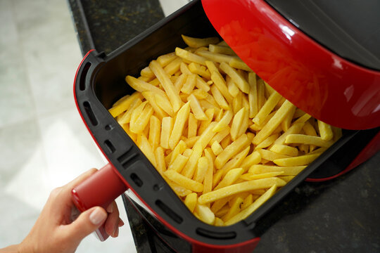 Top-down view of female hand opening air fryer with french fries inside