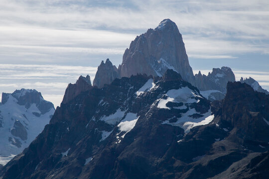 Majestic granite mass of Mount Fitz Roy rising above dark jagged ridges and snowfields under a cloudy sky in Los Glaciares National Park, Patagonia.