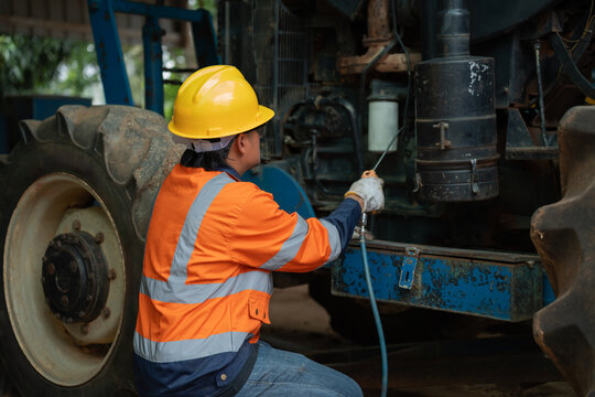 Mechanic services a tractor while wearing safety gear, inspecting and cleaning heavy agricultural machinery during preventive maintenance for reliable farm equipment operation.
