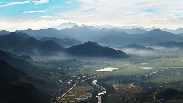 Aerial view of mist-covered mountain ranges and agricultural fields in Guilin, China, bathed in soft morning sunlight under a blue sky.