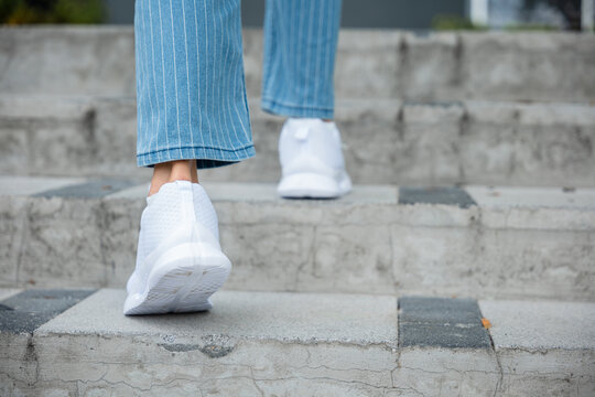 A close-up of a determined young woman's legs in sneakers as she ascends a modern city stairway. Each stepping motion symbolizes her unwavering determination, progress, and the path to success.