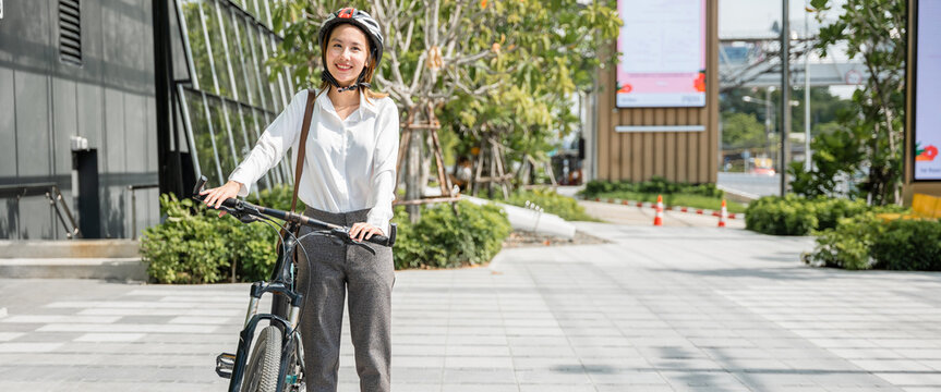 A joyful Asian businesswoman suited up and helmeted stands by her bicycle symbolizing the concept of a modern business commuter. happiness safety and the balance between work and outdoor fun.