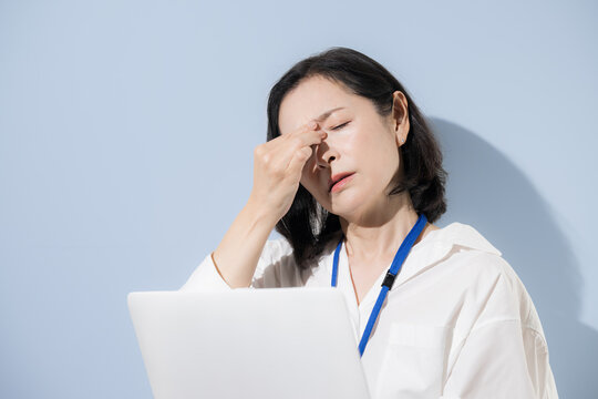 Female office workers suffering from eye strain and eye fatigue; Japanese businesswomen who press the inner corners of their eyes while working on laptops