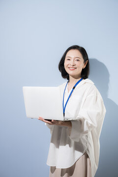 A female office worker smiling while holding a laptop; Japanese businesswomen who leverage digital technology in their work