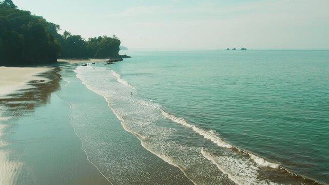 Lone person on empty sandy beach walking in ocean waves in Costa Rica on a sunny day
