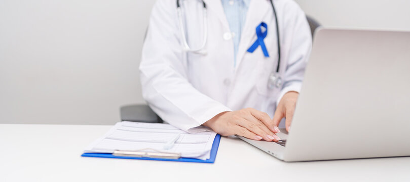 doctor using laptop and report notes on notebook. Navy blue ribbon concept of March Colorectal and Colon Cancer Awareness month, May Arthritis awareness, July Juvenile arthritis and Childhood
