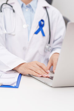 doctor using laptop and report notes on notebook. Navy blue ribbon concept of March Colorectal and Colon Cancer Awareness month, May Arthritis awareness, July Juvenile arthritis and Childhood