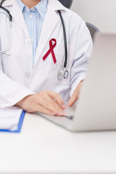 doctor using laptop and report notes on notebook. burgundy ribbon concept of March Multiple Myeloma Cancer Awareness month, September Sickle Cell Anemia, Headache and Migraine week, April Meningitis