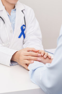 doctor holding patient hand to comfort and support with empathy. Navy blue ribbon concept of March Colorectal and Colon Cancer Awareness month, May Arthritis awareness, July Juvenile arthritis