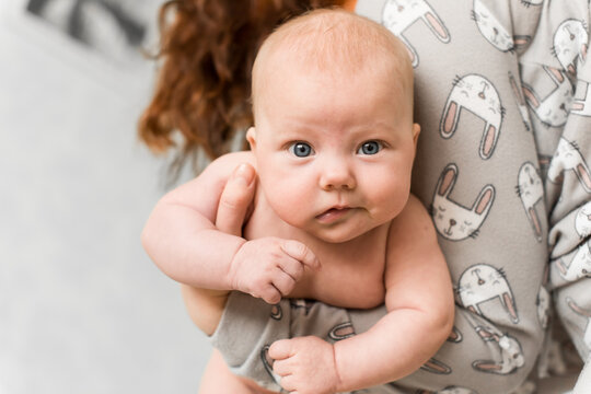 Mother holds and supports baby 5-6 months old at home while the child looks at camera, natural scene of care and motherhood