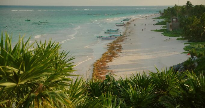 Boats line sandy beach beside palms and turquoise ocean waves at Playa Santa Fe Tulum Mexico
