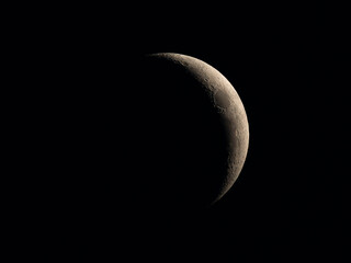 A thin crescent Moon against the dark night sky, with sunlight revealing the craters and rugged surface along the lunar terminator. © Dmytro