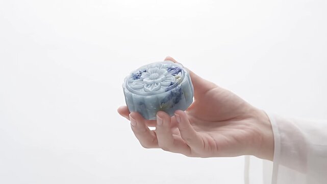Floral embossed blue mooncake held by hand against minimalist white background for Mid-Autumn Festival