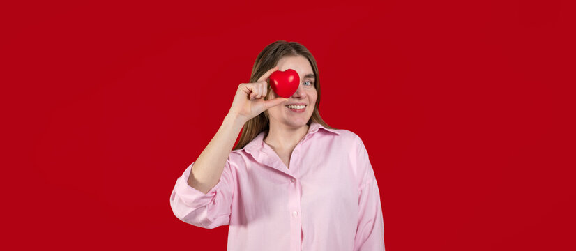Young happy woman holds heart against red background. Copy space banner