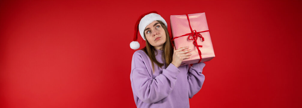 Christmas studio shot of puzzled woman with a gift against red background. Copy space banner 