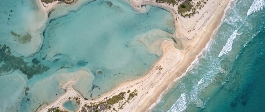Aerial view of a sandy beach coastline with turquoise lagoon waters, white surf waves, and shallow tidal pools along the shore, captured from a altitude perspective