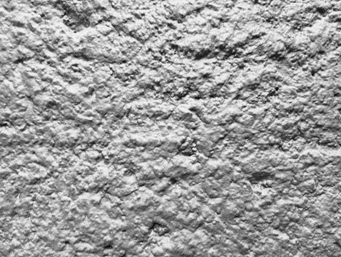 A black and white close-up texture of a rough plaster wall surface covered with thick paint coating. 