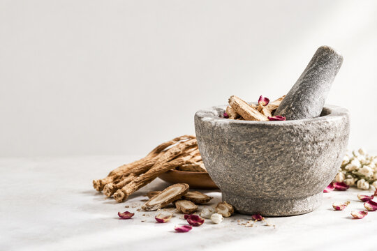 Stone mortar and pestle with dried mandrake roots and petals, herbal apothecary still life