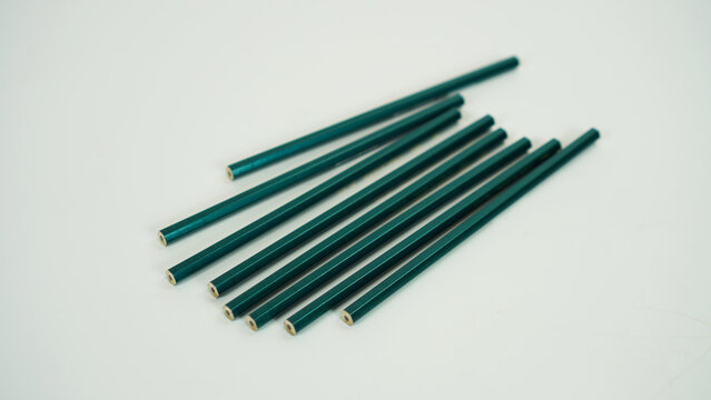 Eight unsharpened bottle-green pencils lying in a haphazard arrangement against a white background.