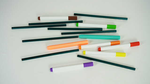 Several colorful markers and pencils scattered on a white background, children's education concept, children's school equipment,