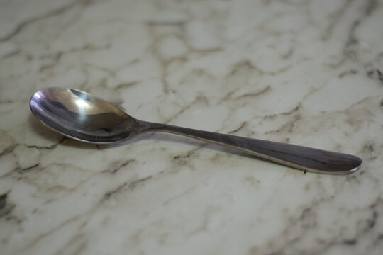 Single small stainless steel teaspoon lying diagonally on a marble countertop surface