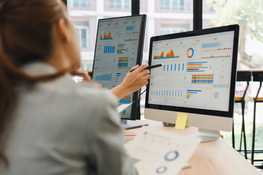 Businesswoman pointing at statistical charts and financial data on desktop computer screen in office