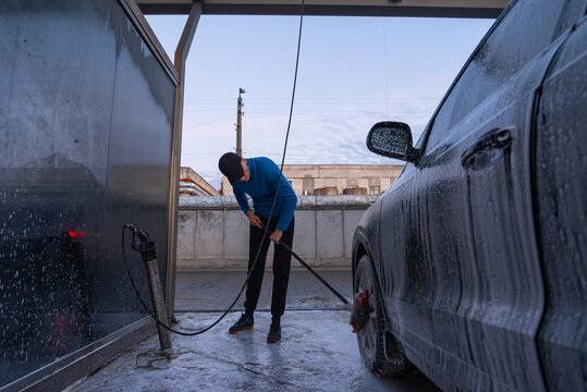 After sunset dark time Concept of vehicle maintenance, car care, cleanliness transportation and modern automated washing services. Man Washing Car at Self Service Car Wash Using Foam Cleaning System