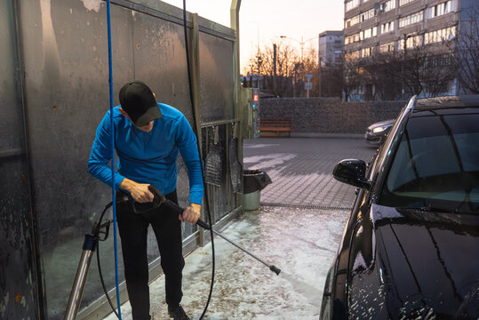 Blue hour dark light Man cleans his vehicle at self service car wash station using professional washing equipment. Rinsing the vehicle with high-pressure water stream system. Outdoor washing bay with
