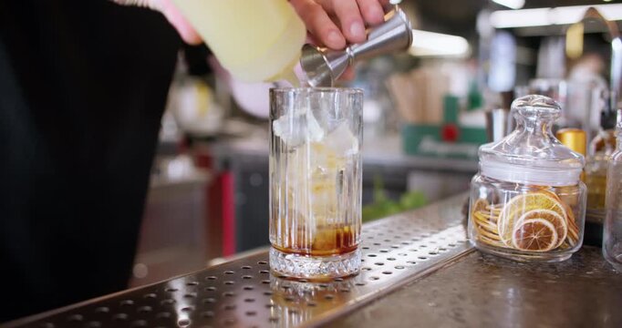 Mixing cocktail. Measuring ingredient. Bartender hand pouring syrup for cold alcoholic drink from metal jigger to cold ice cube glass.