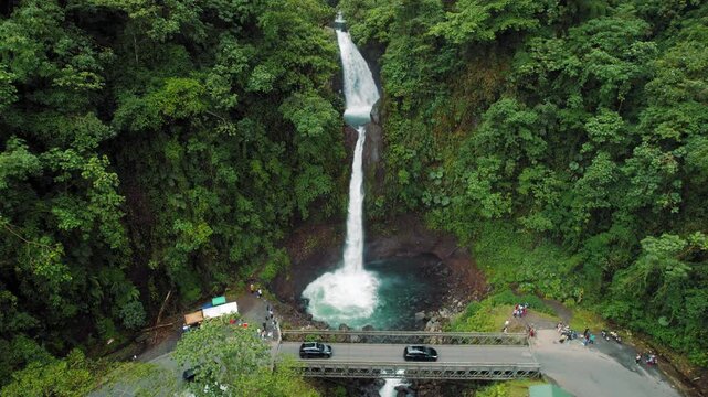 La Paz waterfall dropping beside bridge surrounded by rainforest and visiting tourists