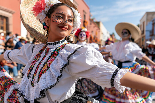 Brightly dressed dancer smiles during colorful parade. Face painted, adorned with floral hat and lace blouse. Dance moves suggest joy and cultural celebration