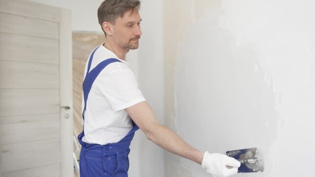 Skilled plasterer spreading smoothing compound over wall surface, leveling imperfections with professional technique, creating flawless backdrop for interior finishing